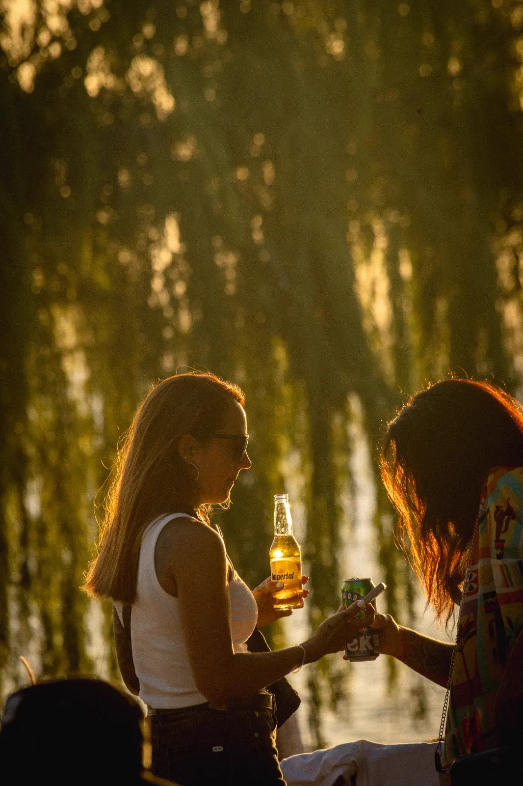 Dos amigas brindando a contraluz entre los sauces, frente al lago